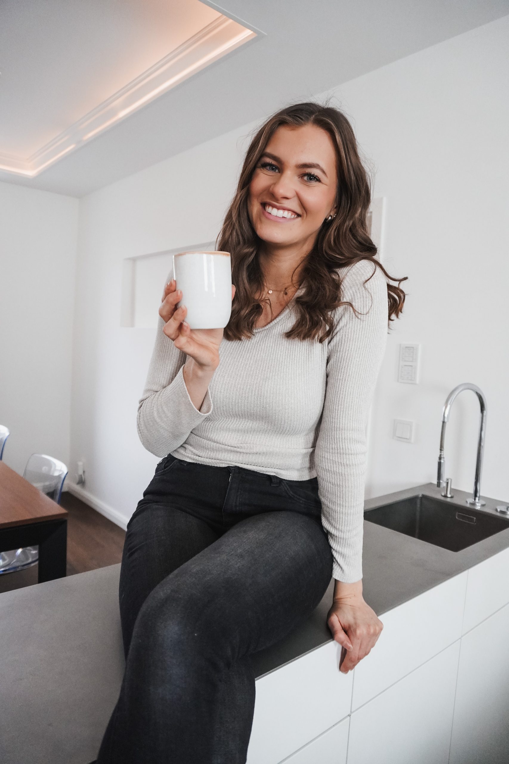 Portrait von mir, Lisa-Marie, sitzend auf einem Küchentresen und entspannt eine Tasse Kaffee oder Tee genießend.