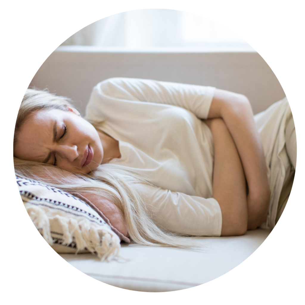 Frau liegt mit Schmerzen auf der Couch und hält sich den Bauch als Sinnbild für Blähungen und Verstopfung welche mit Hilfe von Ayurveda Beratungen behandelt werden kann.